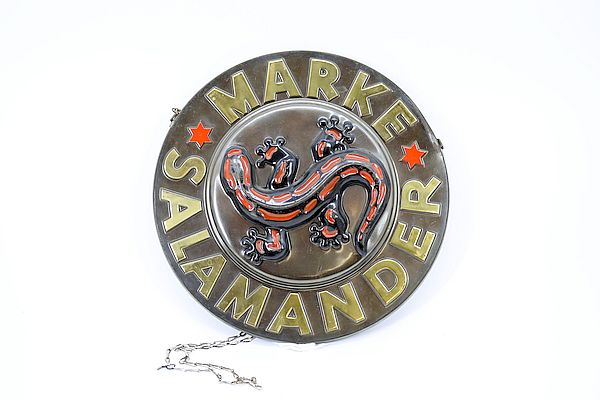 Rundes, emailliertes Werbeschild mit einem roten Salamander in der Mitte und der Aufschrift „Marke Salamander“ in goldenen Buchstaben, zwei rote Sterne auf weißem Hintergrund. Foto: Stadt Kornwestheim.